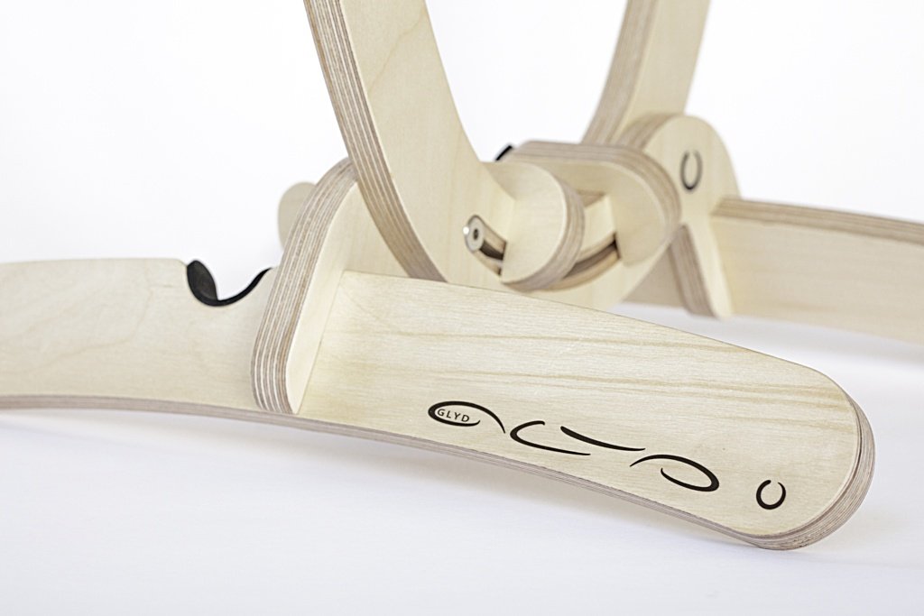 Close up cropped image showing curved wooden foot in foreground made from clear varnished birchwood with GLYD O name and Logo showing prominent on this front facing foot. In the background you can see the tail holders, other foot and bottom of the cradle, Image is taken on a 45 degree angle. Transparent background.