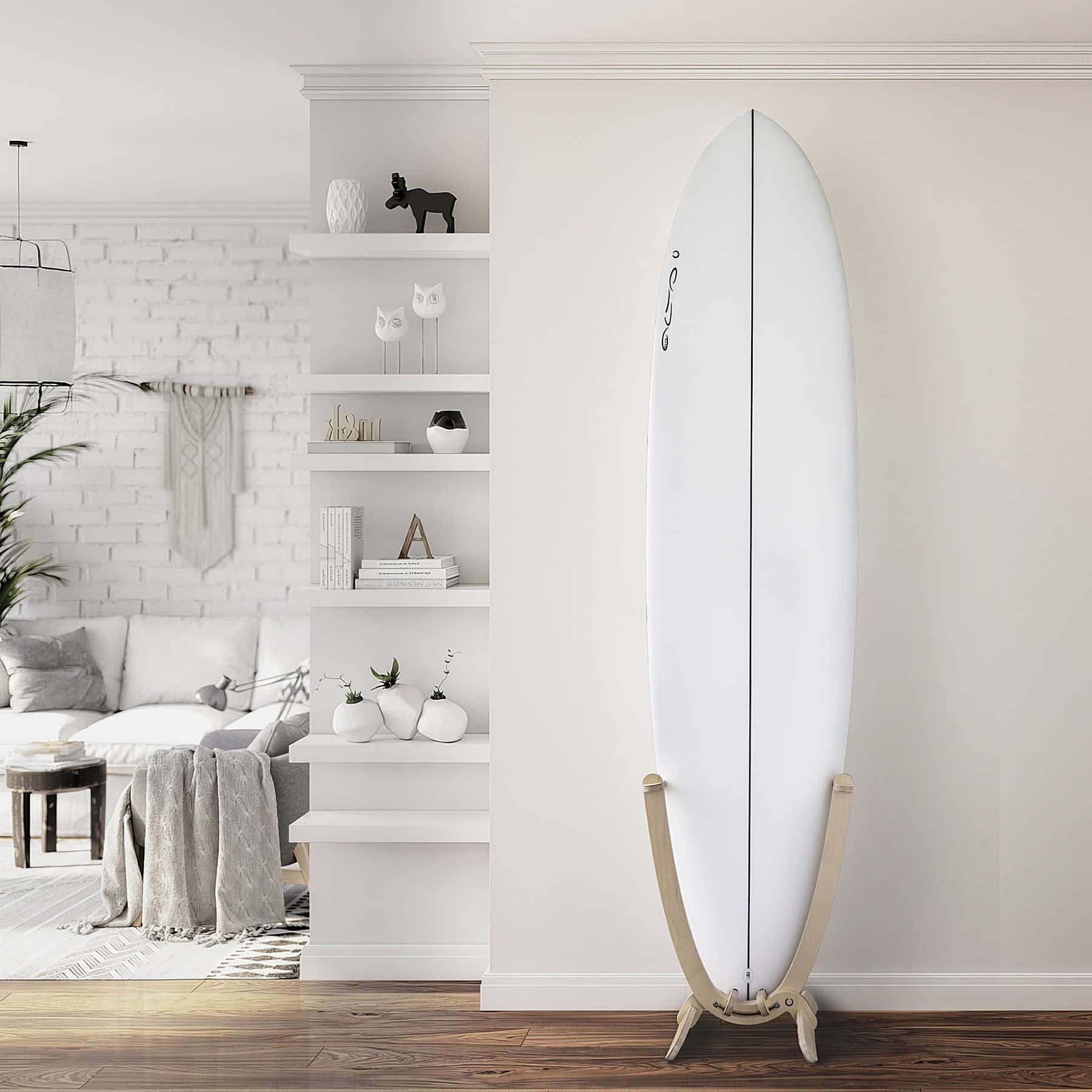 An all white Surfboard with a GLYD O decal on its nose, is mounted in a GLYD O surfboard rack. The rack with board is standing on a wooden floor against a flat white wall. The room opens up to the left of the rack and board, there are inset shelves on the corner of the flat white wall with ornaments, books and small plants. Around the corner there is a white brick wall a couch, small coffee table, Lamp, wall hanging, plant and hanging light. The surfboard rack and surfboard really pop in this picture and the image gives you an idea of the feeling and vibe the GLYD O surfboard rack brings to a room. The Surfboard Rack is a Beautiful birchwood curved single surfboard rack in the shape of the tail of a surfboard, with hooks to hold the rails and tail and two slightly curved feet connected perpendicular to the upright curved arms. Image is taken from the front in relations to the vertical surfboard rack.