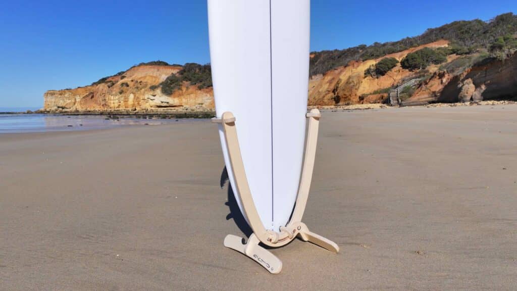 GLYD O Revolute Board Rack close up image, with surfboard mounted, standing on beach. Ocean and cliffs in background.
