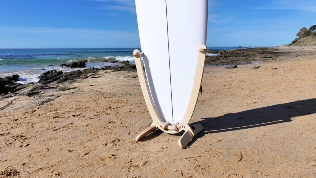 GLYD O Revolute Surfboard Standing Rack close up image, with surfboard mounted, standing on beach. Lorne Point, Ocean and Jetty in background.
