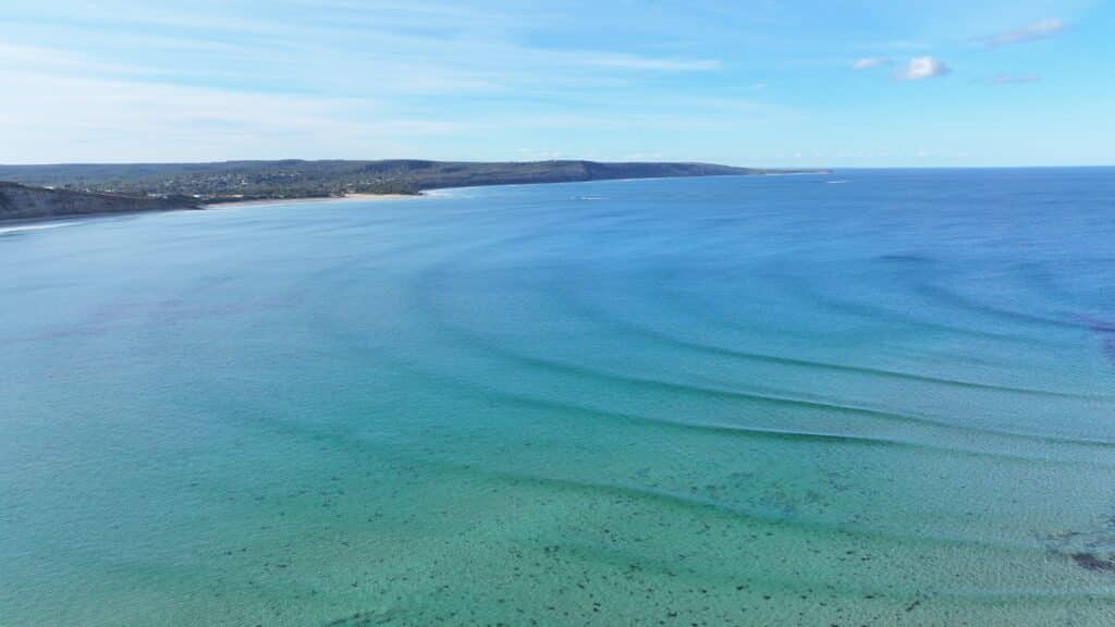 Aerial view of Point Roadnight bay looking east toward Anglesea and distant Point Addis showing vast turquoise waters with corrugated ocean swells curving along Victorian coastline.