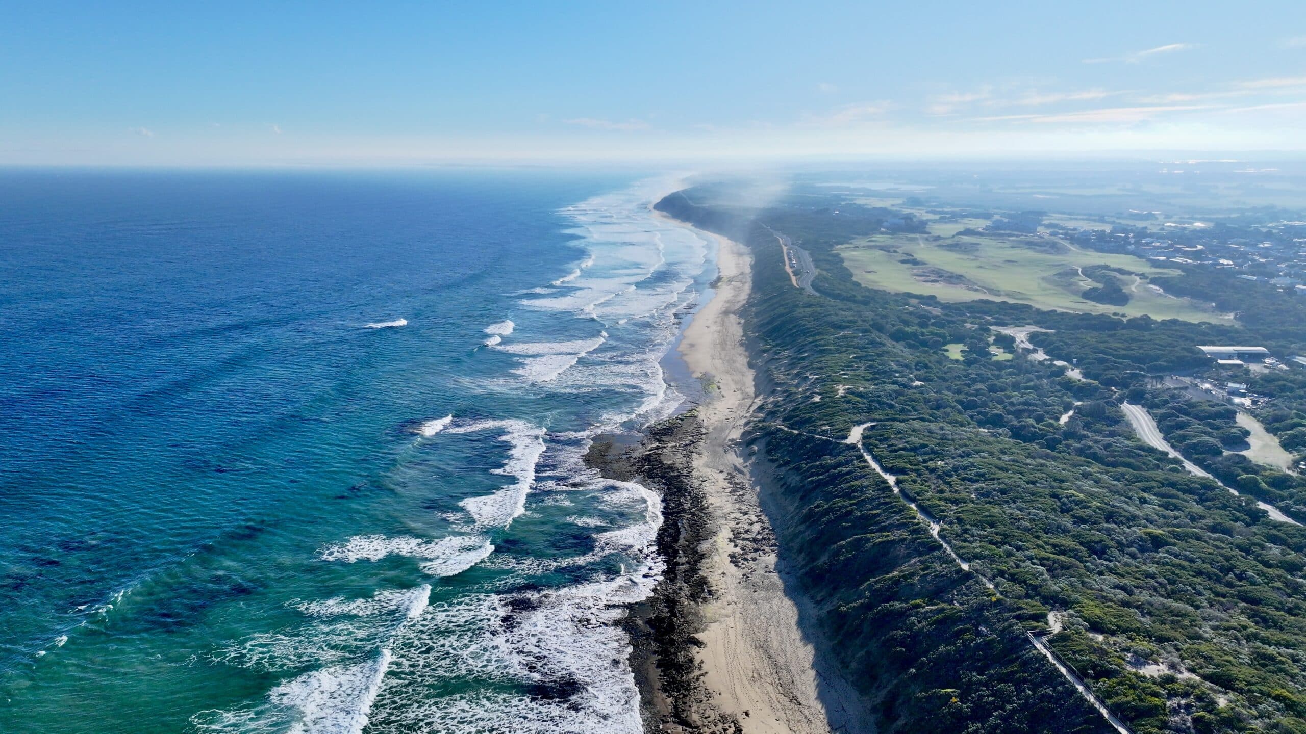 Aerial view above The Bluff looking west over 13th Beach toward Point Impossible and Torquay with coastal vegetation and golf course.
