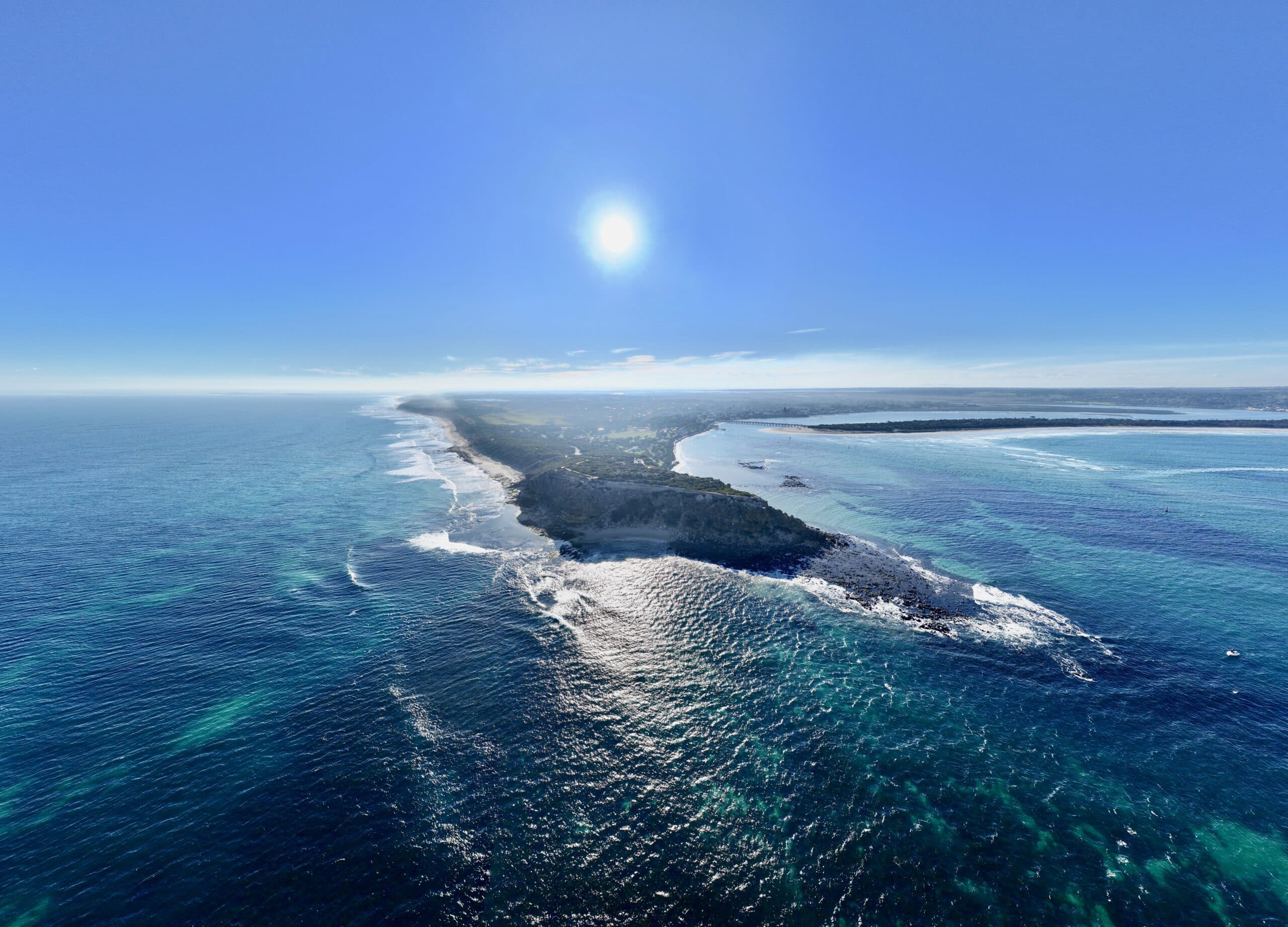 Aerial view of The Bluff Barwon Heads from 120 meters showing coastline, 13th Beach, and Barwon River mouth. Sun low in the sky. Wooden board rack on beach.