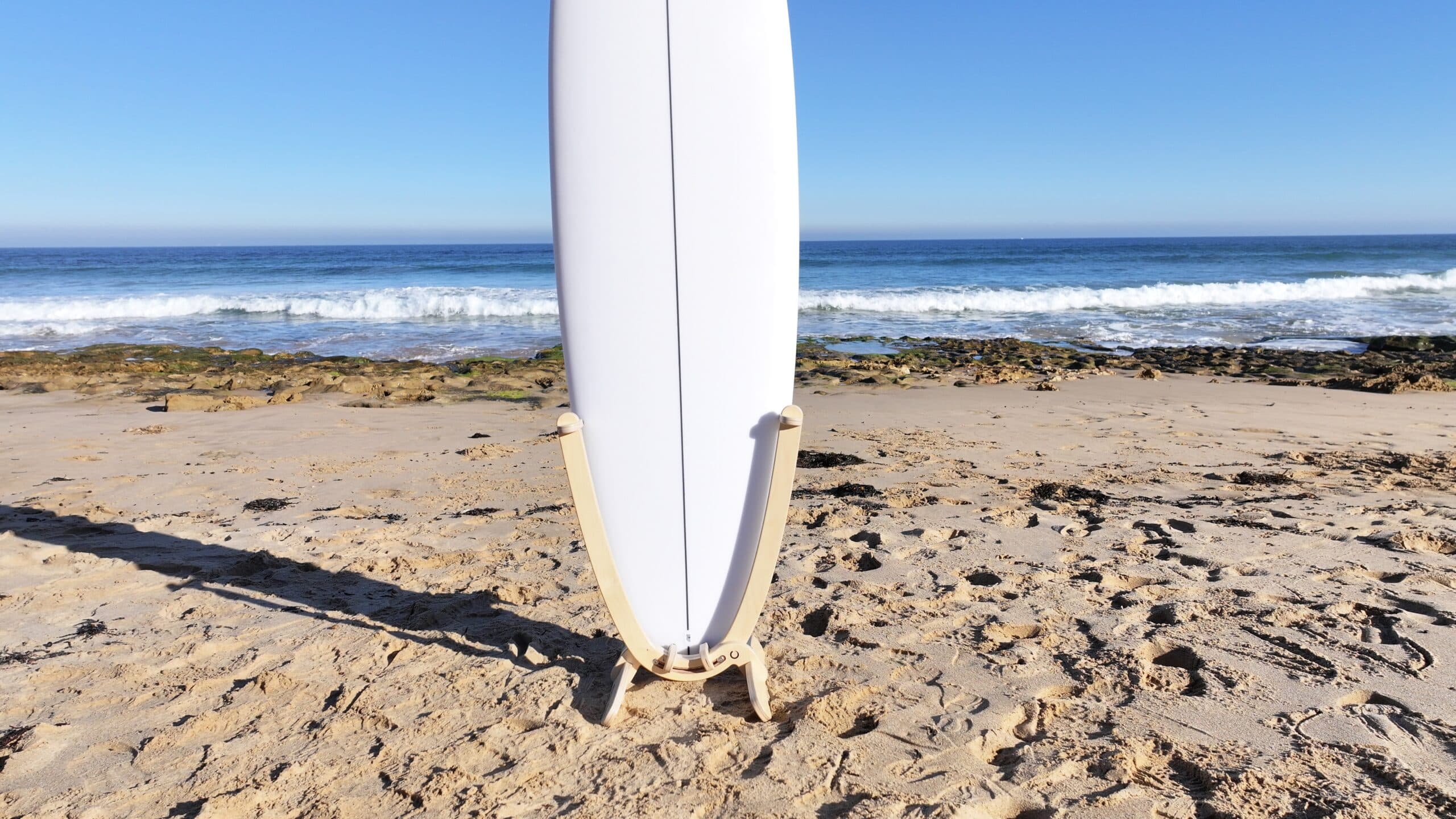 Close-up view of wooden board rack holding white surfboard on beach sand at The Bluff Barwon Heads.