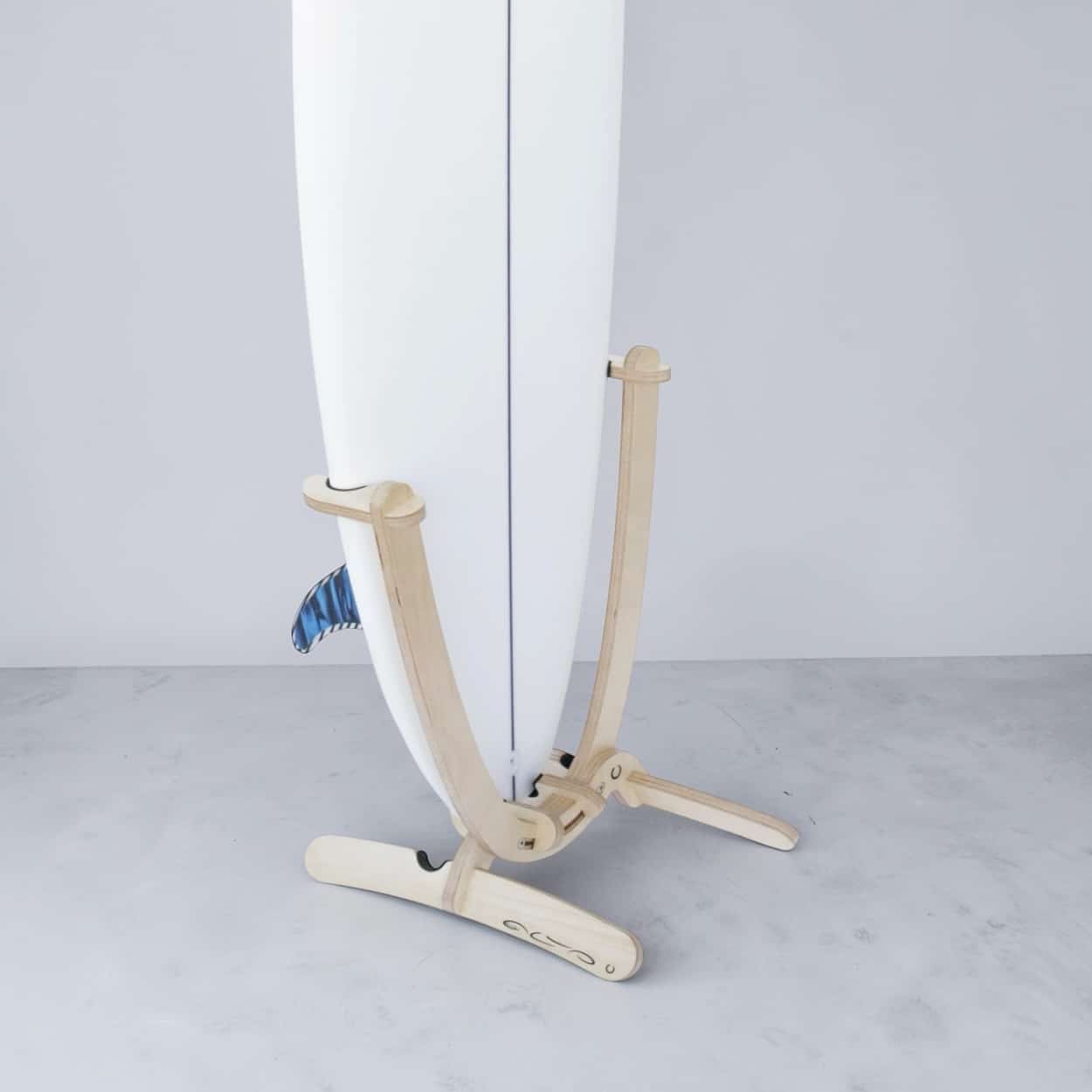 Wooden Revolute surfboard rack made from sustainable birch plywood holding a white surfboard upright.